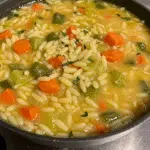 Easy Orzo Vegetable Soup 5 Bowl of homemade orzo vegetable soup with visible pasta, chickpeas, white beans, carrots, and green kale in clear vegetable broth, served with crusty bread