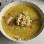 Bowl of chicken and rice soup with carrots, celery, and herbs