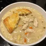 Chicken Pot Pie Soup 6 A bowl of creamy chicken pot pie soup with tender chicken, carrots, peas, and herbs, served with a warm biscuit